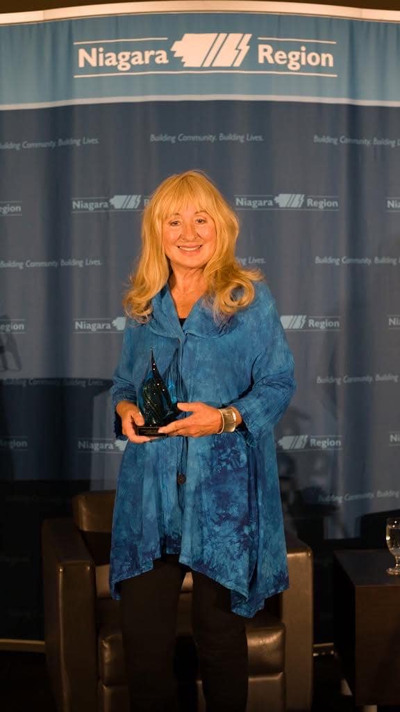 Accepting the Niagara Impact Award for Stockings of Love in front of a Niagara Region banner