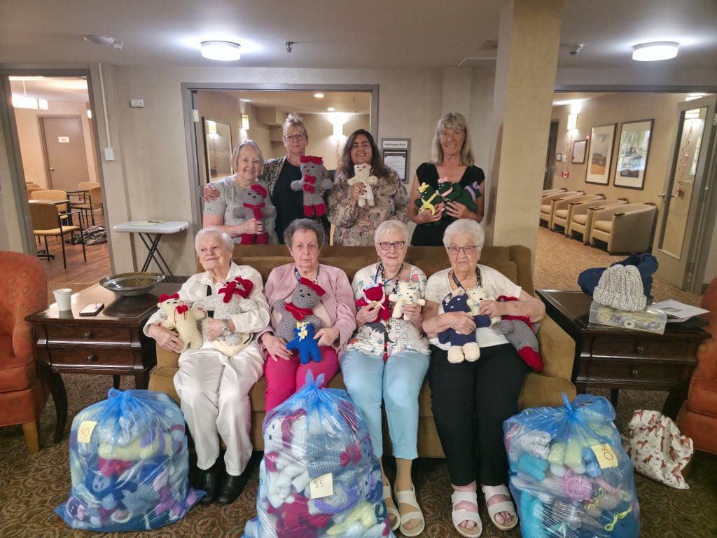 Volunteer Elves and seniors together holding hand-knitted teddy bears